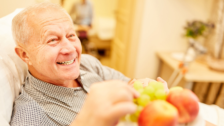 Senior nimmt einen Apfel vom Teller einer Pflegerin Senior nimmt einen Apfel vom Teller einer Pflegerin